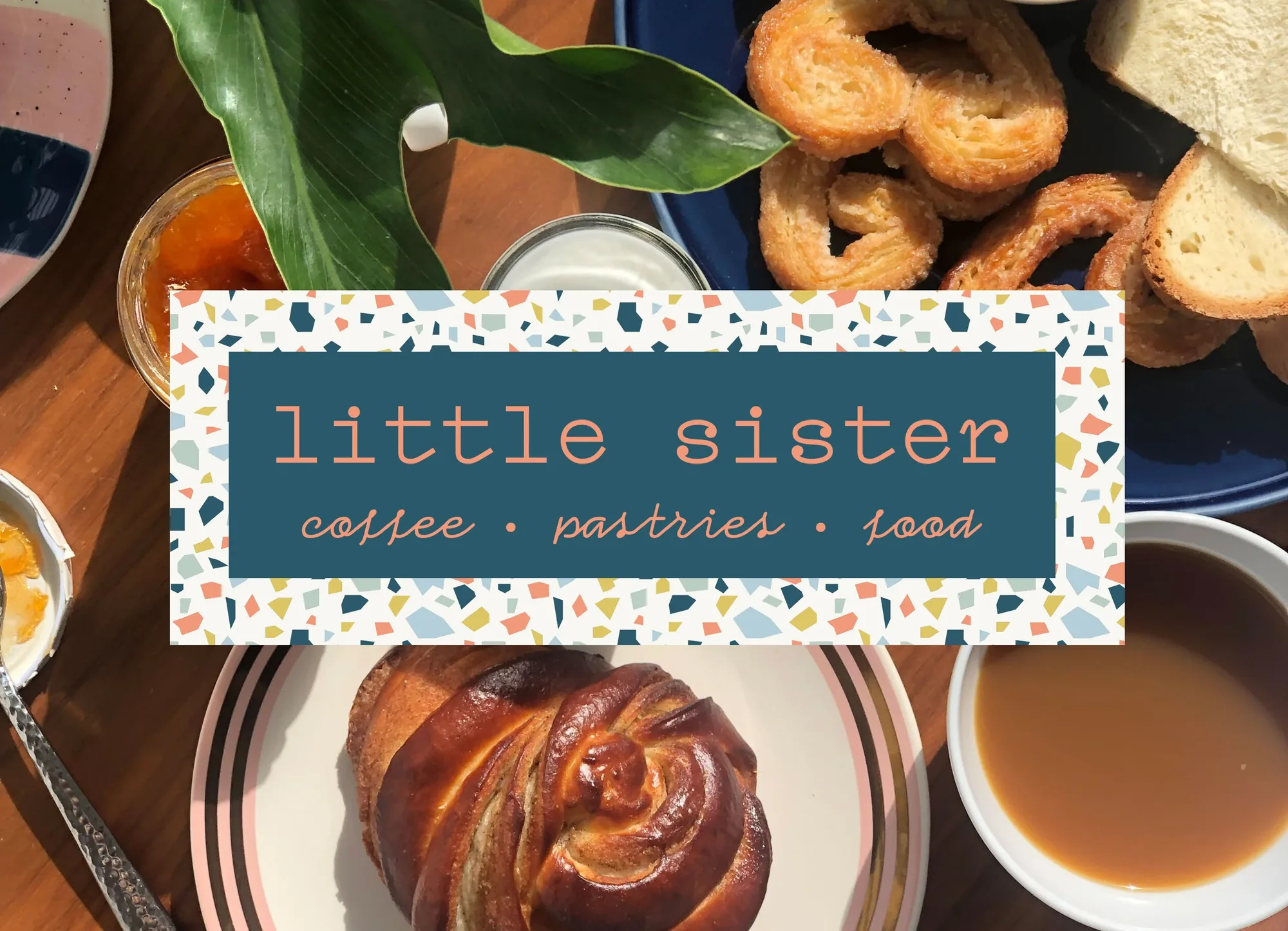 A glazed pastry swirl on the striped plate, with palmiers, bread, jam and coffee on the café table
