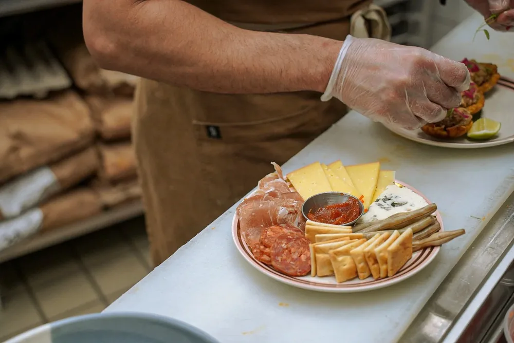 A chef in a brown apron plating a board of cured meats and cheese