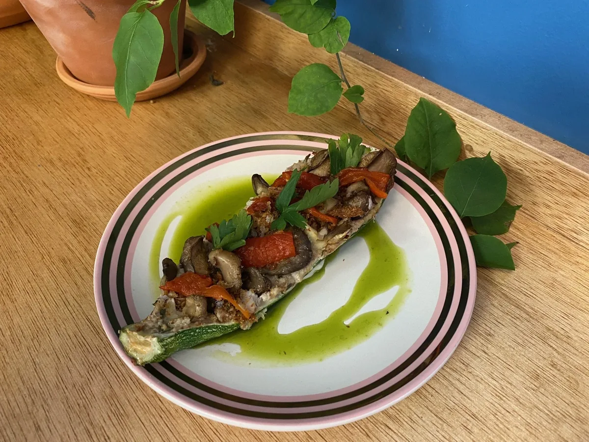A stuffed zucchini on a pink-and-black striped plate on an oak table against the café’s blue wall
