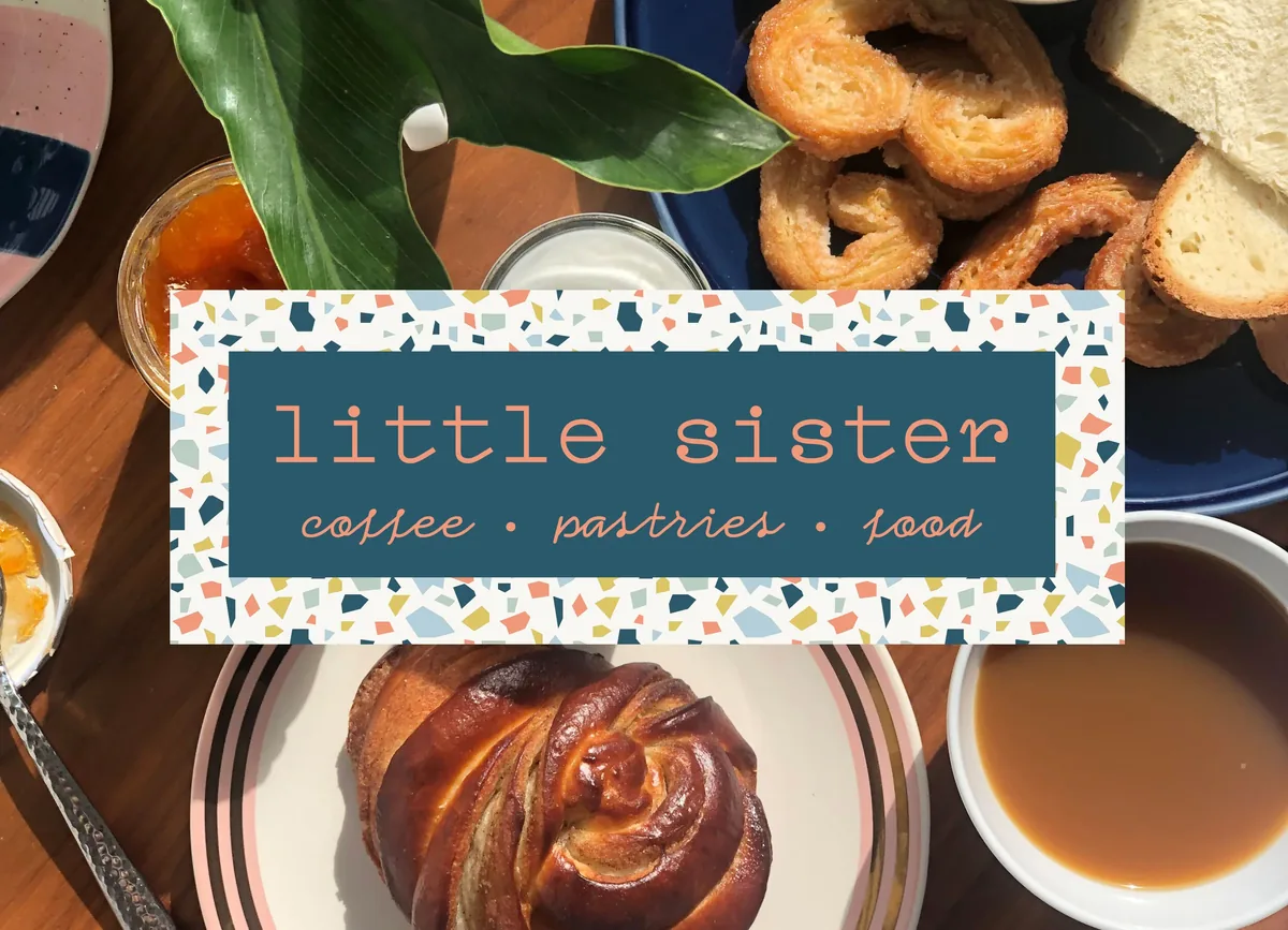 A glazed pastry swirl on the striped plate with palmiers, bread, jam and coffee, under the Little Sister sign