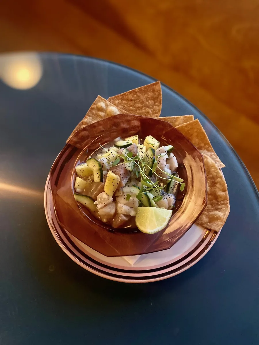 Ceviche in an amber glass bowl with chips on a dark table in warm light