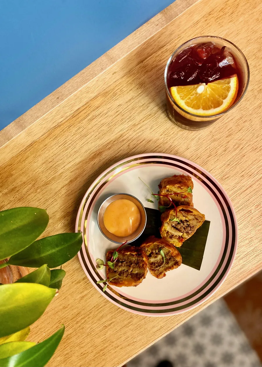 Fried bites with dipping sauce on a pink-and-black striped plate beside an iced drink, from above